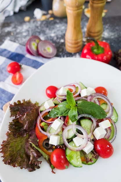 Greek salad on a white plate on dark stone background. Fresh food flat lay.