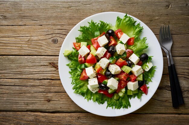 Greek salad on white plate on old rustic wooden table top view copy space