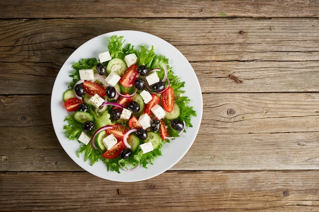 Greek salad on white plate on old rustic wooden table, top view, copy space