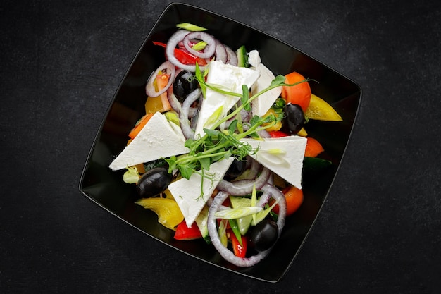 Greek salad with cheese and vegetables on a black plate