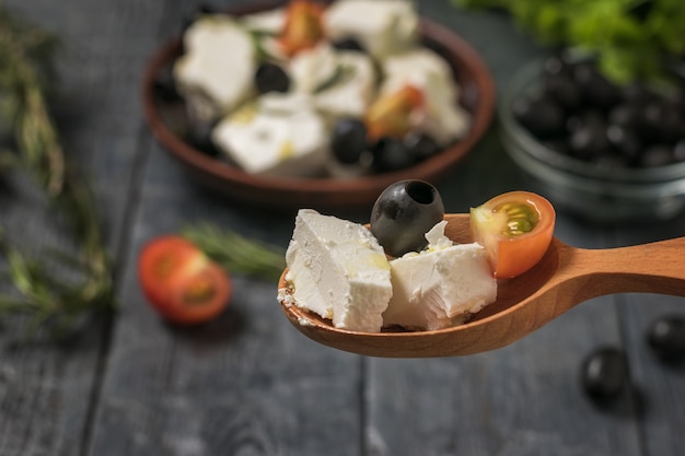Фото Греческий салат с сыром фета в деревянной ложке. салат с сыром и овощами.