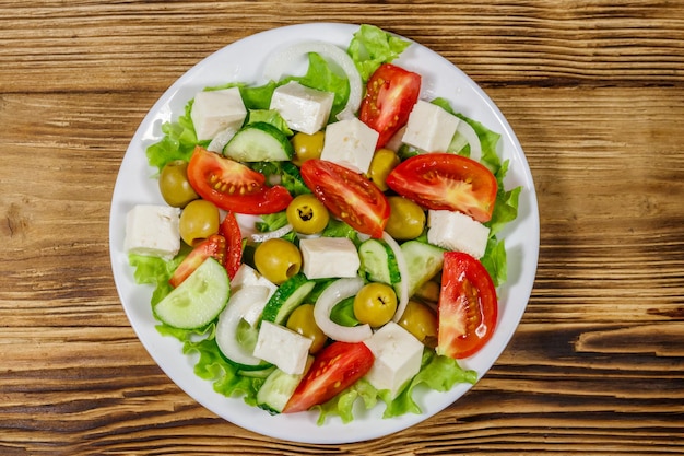 木製のテーブルに新鮮な野菜のフェタチーズとグリーンオリーブのギリシャ風サラダ上面図