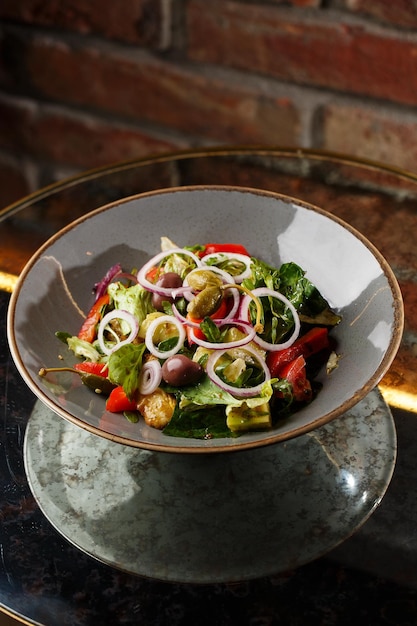 Greek salad with fresh vegetables tomato cucumber red bel pepper lettuce onion olives and cheese Closeup on a white round plate on a wooden background Salad menu with ingredients