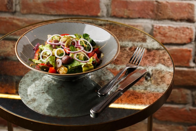 Foto insalata greca con verdure fresche pomodoro cetriolo peperone rosso lattuga cipolla olive e formaggio primo piano su un piatto rotondo bianco su fondo di legno menu di insalata con ingredienti