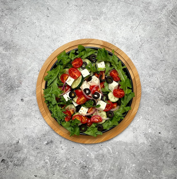 Greek salad with tomatoes cucumbers olives feta cheese herbs in a plate on a light background