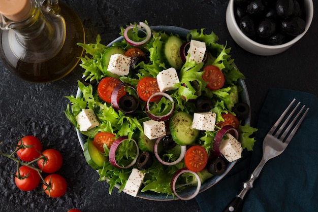 Insalata greca con pomodori, cetrioli, olive e formaggio feta in un piatto su fondo di cemento, vista dall'alto