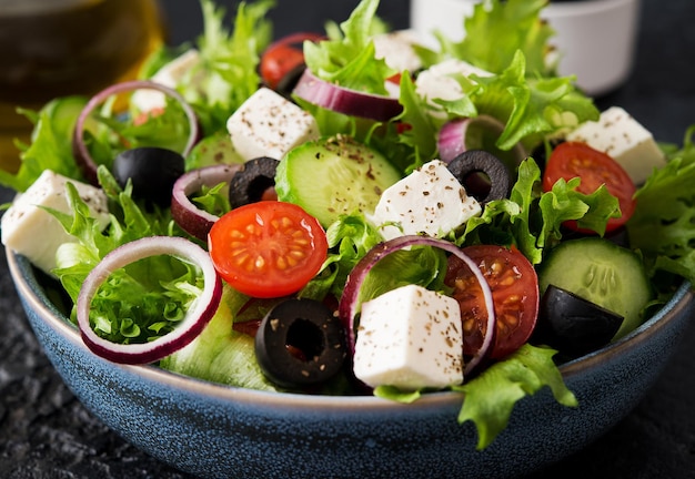 Insalata greca con pomodori, cetrioli, olive e formaggio feta in un piatto su fondo di cemento, cucina greca tipica, primo piano