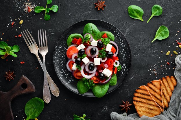 Greek salad with tomatoes paprika onions and feta cheese In a black plate on a wooden background Top view Free space for your text Flat lay