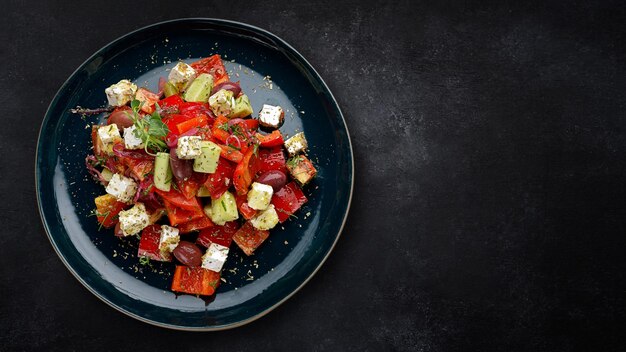 Greek salad with vegetables olives and cheese on a dark plate on dark concrete