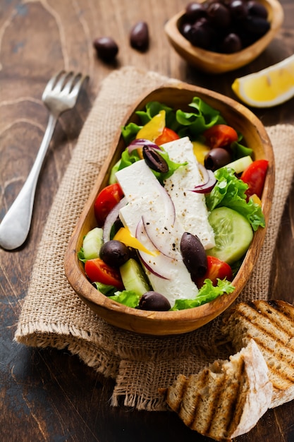 Greek salad in wooden plate on old wooden background