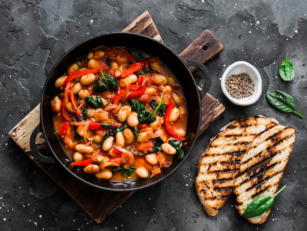 Greek style tomato sauce spinach paprika beans stew in a cast iron pan on a rustic board on a dark background top view Simple comfort food