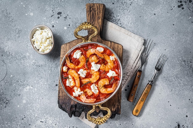 Greek traditional oven backed prawns shrimp saganaki with feta tomato paprika and thyme Gray background Top view