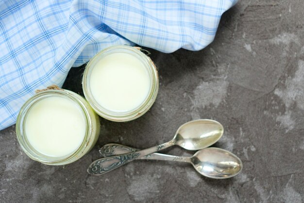 Greek yogurt in glass jars with spoons on a gray background. Top view. Copy space.