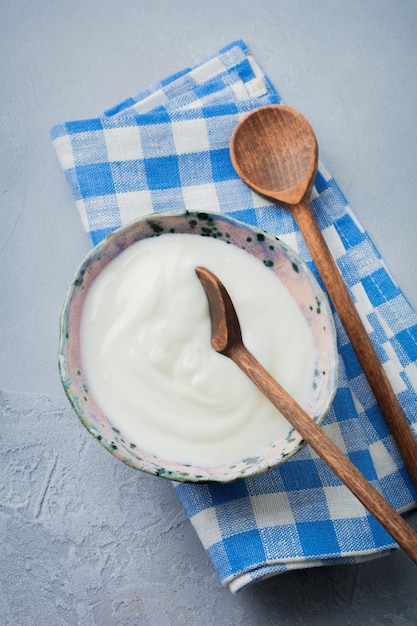 Фото Греческий йогурт в керамической тарелке с деревянными ложками на серой бетонной поверхности