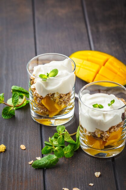 Greek yogurt mango granola parfait in a glass on dark wooden background.