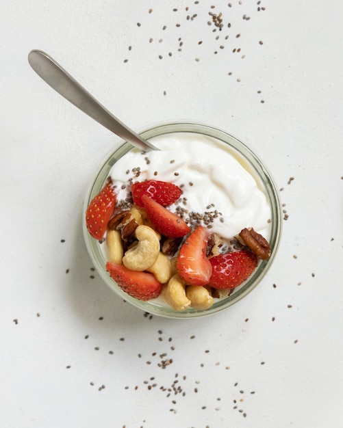 Greek yogurt nuts and strawberries in a glass jar with a spoon on a white table top view