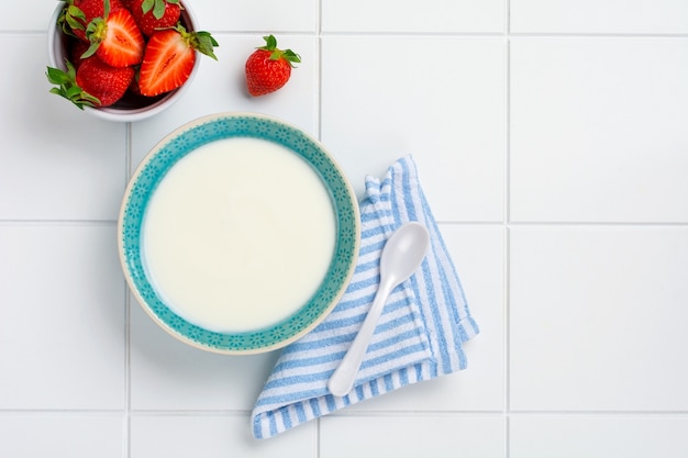 greek yogurt in white bowl with ingredients for making breakfast granola and fresh strawberries