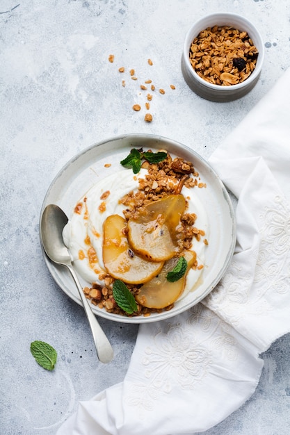 Greek yogurt with caramelized pear, granola, nuts and melted sugar for a wholesome breakfast on a gray ceramic plate. Rustic style. Top view.