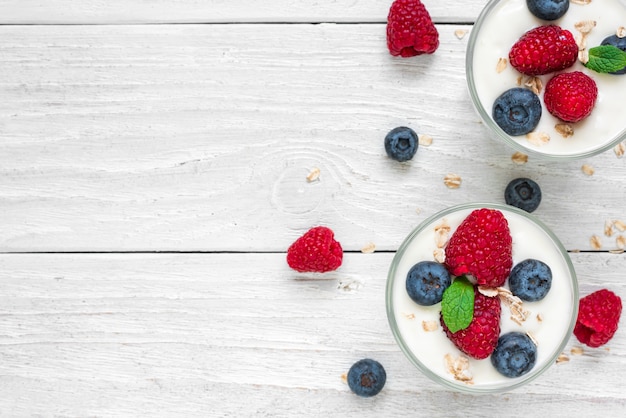 Yogurt greco con frutti di bosco freschi, avena e menta in bicchieri sul tavolo di legno bianco. colazione salutare