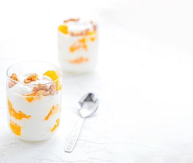 Yogurt greco con arancia e noci in bicchieri su un tavolo bianco cibo sano concetto di alimentazione