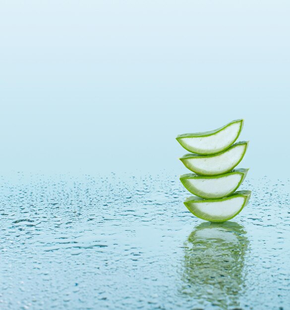 Photo green aloe leaves and pieces of aloe on a blue background with water drops