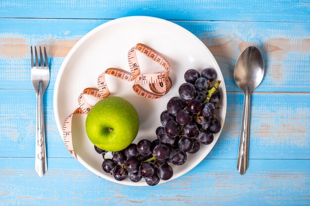 green apple and black grapes in white dish with pink Measuring tape 