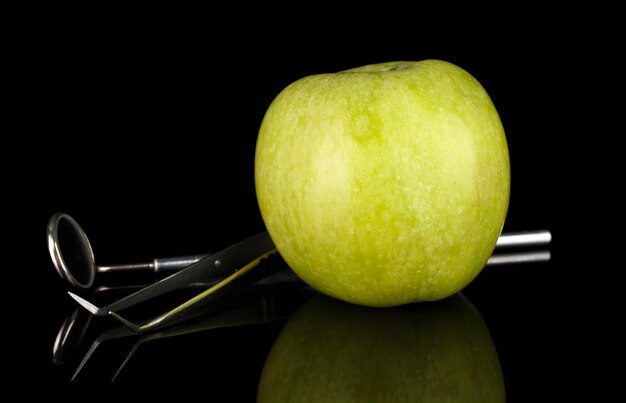 Green apple and dental tools isolated on black