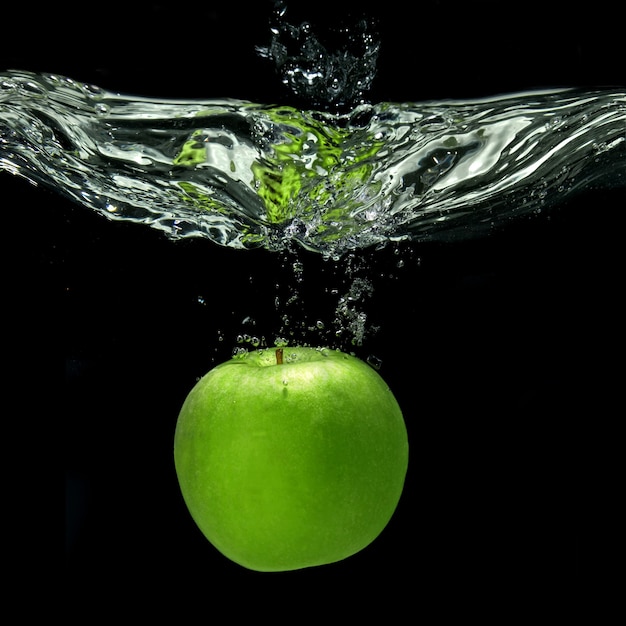 Зеленое яблоко упало в воду с брызгами, изолированными на черном