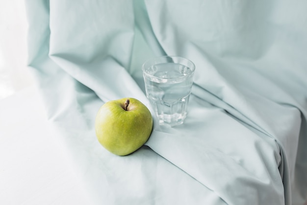 Green apple and a glass of water on a blue towel. Health care and diet concept