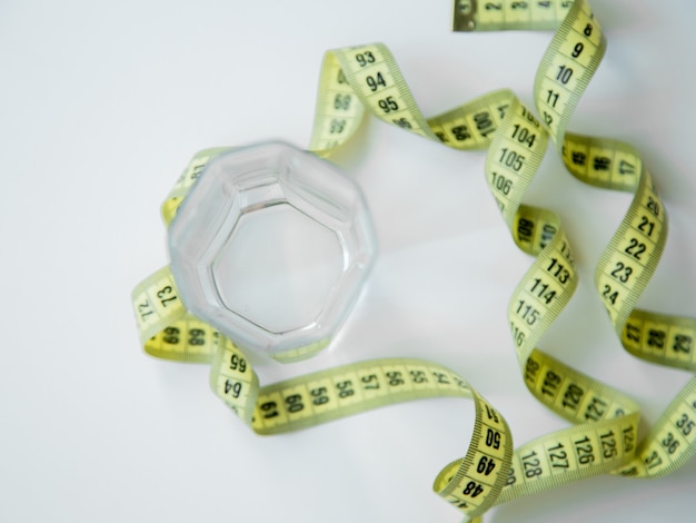 A green apple and a glass of water stand on a white background they are entwined with a measuring ta...