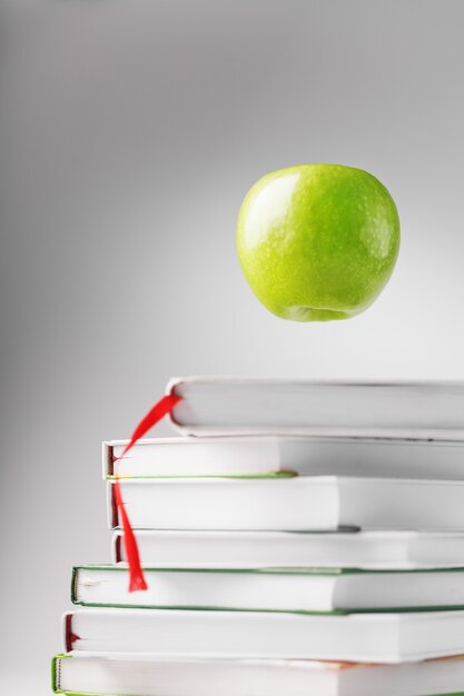 A green Apple hovers over isolate books on a white table.