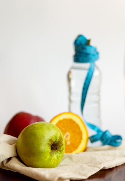 Foto mela verde, arancia e acqua in bottiglia con misurazione nastro blu su sfondo bianco, concetto di stile di vita sano.