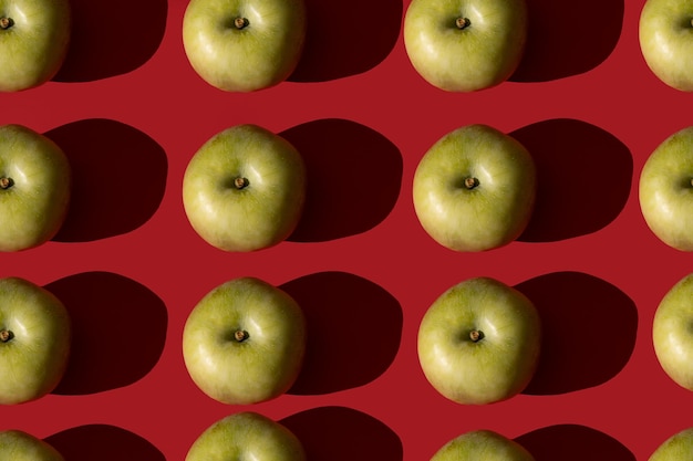 Photo green apple. pattern of green apples on a red background with hard shadows. top view.
