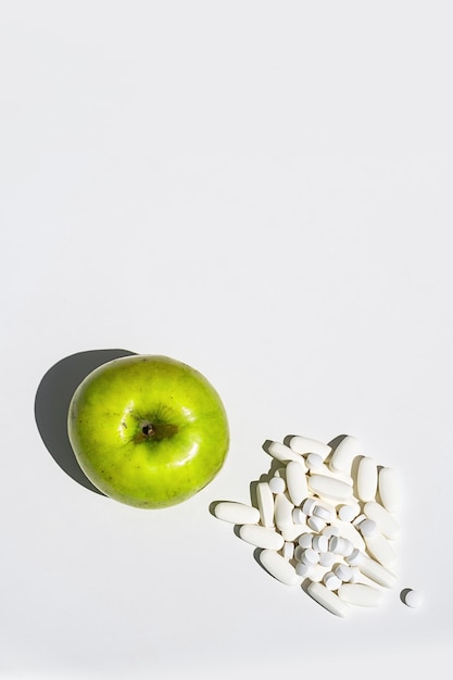 Green apple and pills or vitamin capsules on white table copy space Wellness diet or supports for health concept