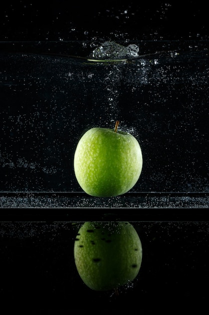 Foto mela verde che spruzza nell'acqua su fondo nero.