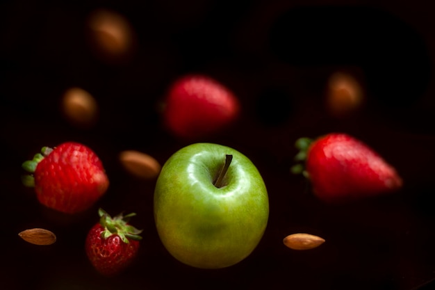 Green apple strawberries and almonds floating on black background nutrition concept