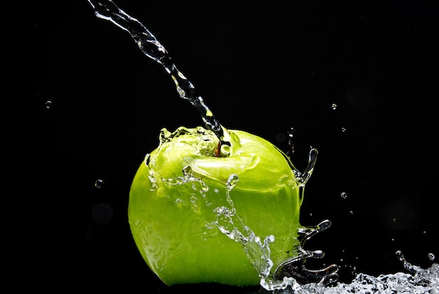 Green apple with water splash on black wall