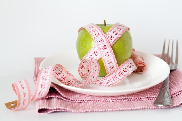 Green apple wrapped in a tape measure on a white plate and a pink napkin on a white background