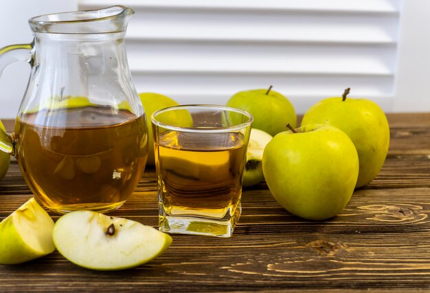 Green apples and jug with glass with apple juice on wooden background
