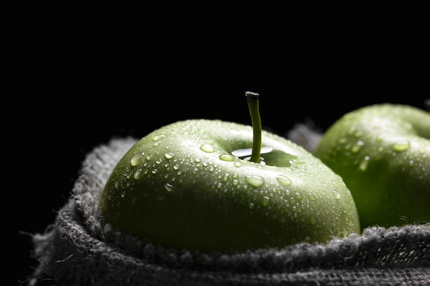 Green apples in a jute bag with water drops on a dark wall