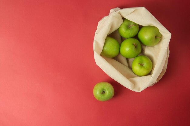 Green apples in white tote bag, red background. Zero waste concept. 