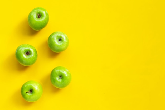 Green apples on yellow background. Copy space