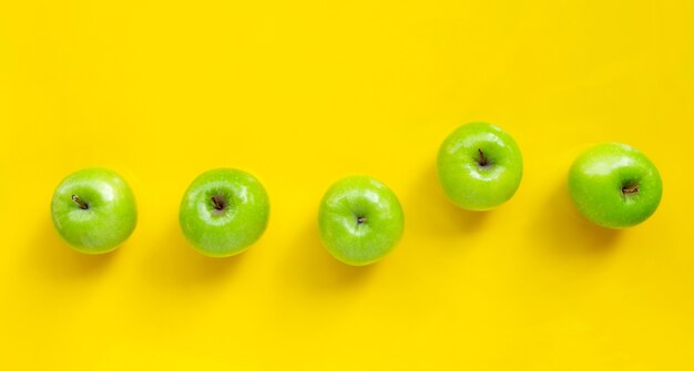 Green apples on yellow background. Copy space