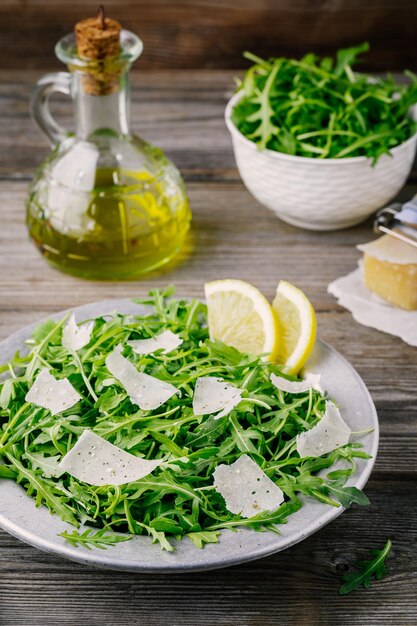 Зеленый салат из рукколы с сыром пармезан, лимонным оливковым маслом и приправами на деревянном фоне