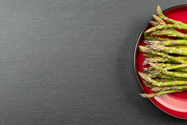 Green asparagus on a black slate stone background. Top view, asparagus in a red plate. Culinary banner with place for text.