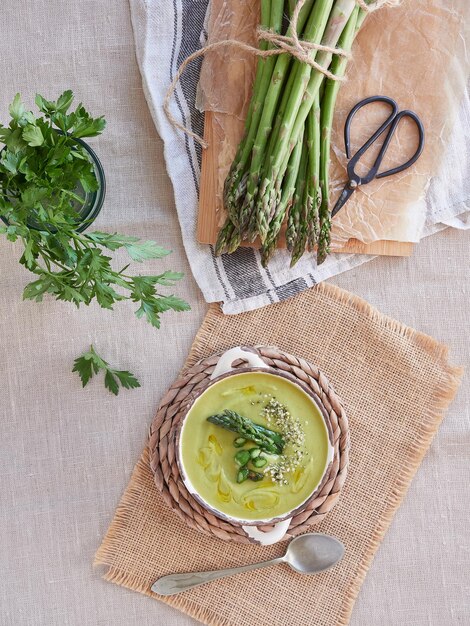 Green asparagus cream soup served in a bowl beside a bunch of fresh wild asparagus and parsley