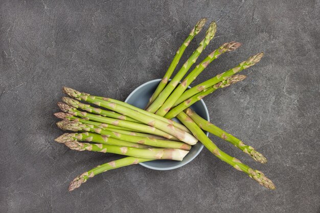 Green asparagus in gray ceramic bowl. Black background. Flat lay