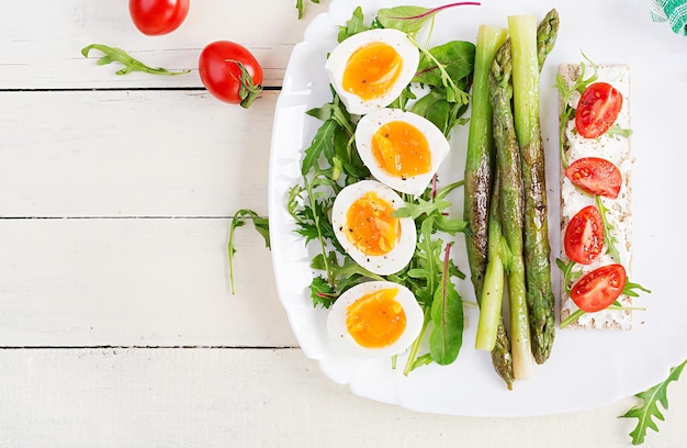 Green asparagus with boiled eggs and sandwich cream cheese on a white plate Top view flat lay