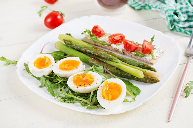 Green asparagus with boiled eggs and sandwich cream cheese on a white plate