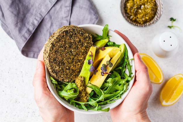 Insalata di avocado verde con cotoletta vegana verde, rucola e pesto in mano. concetto di cibo sano vegano.